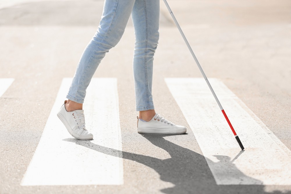 A visually impaired person is crossing the street with a white cane.